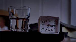 Glass of water next to clock on nightstand in middle of the night
