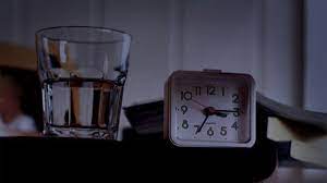 Glass of water next to clock on nightstand in middle of the night